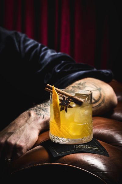 Punch cocktail held in a moody bar setting with red curtain