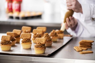 Chef piping Biscoff cream onto mini cupcakes on a production tray