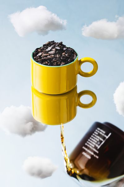 Coffee pouring into stacked cups with cloud styling, surreal concept shot