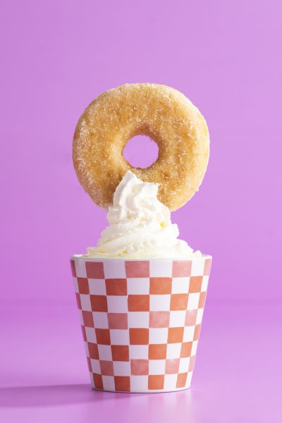 Sugar donut balanced on a whipped cream cup, pink backdrop